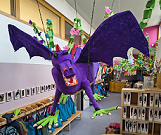 Ein gebastelter Drache aus Pappmaschee in lila mit grünen Füßen schwebt von der Decke im Eingangsbereich der Kindertagesstätte Sonnenwelle