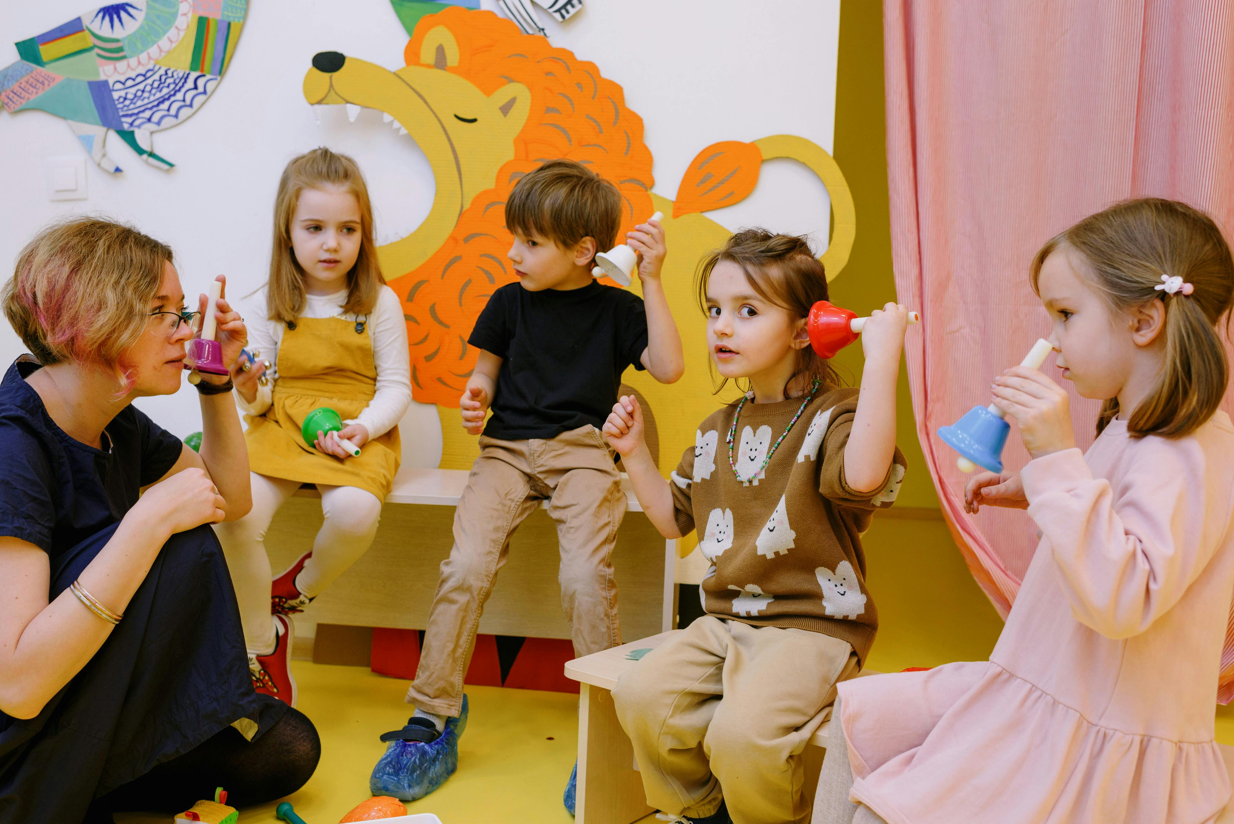 Foto von einer Frau und vier Kinder im Kindergartenalter, die bunte Glocken in der Hand haben und sich an die Ohren halten
