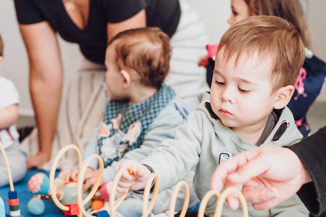 Pexels-Foto auf dem drei Kleinkinder auf einem Teppich spielen und im Hintergrund eine Frau auf dem Boden kniet
