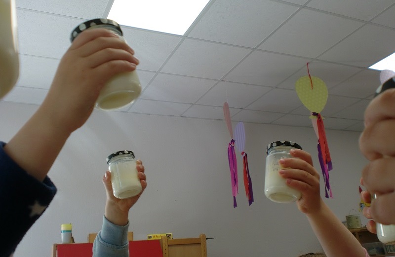 Kinderhände halten kleine Gläser mit Schraubverschluss hoch, sie schütteln darin Sahne zu Butter