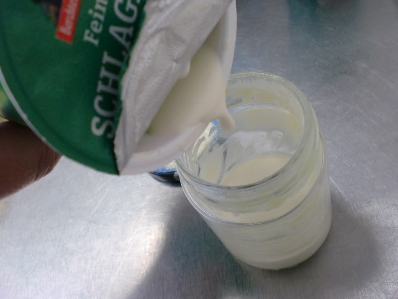 Sahne wird aus einem grünen Plastikbecher in ein Glas gefüllt