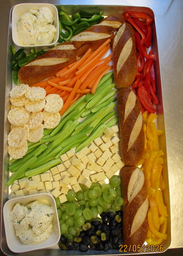 große Schale mit klein geschnittenem Paprika, Trauben, Gurken, Möhren und Puffreis, Frischkäse und Laugenstangen