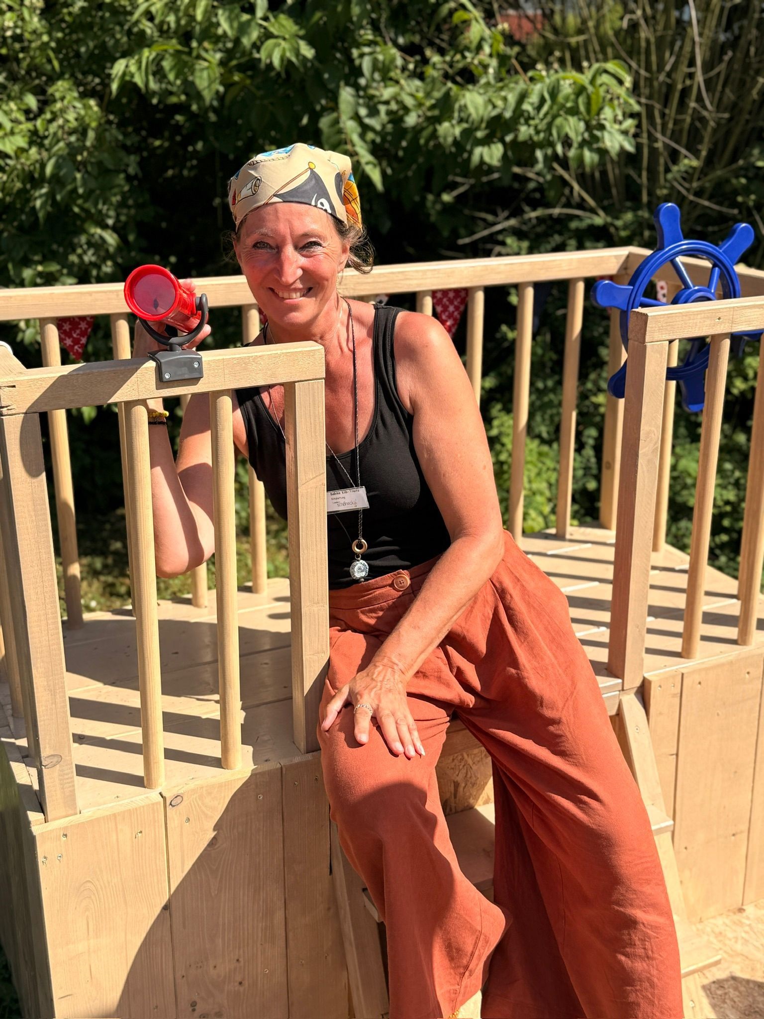 Die Kita Leitung Sabine Kilb-Treitz sitzt auf einem Spielschiff aus Holz und lacht, sie trägt eine Piratenmütze