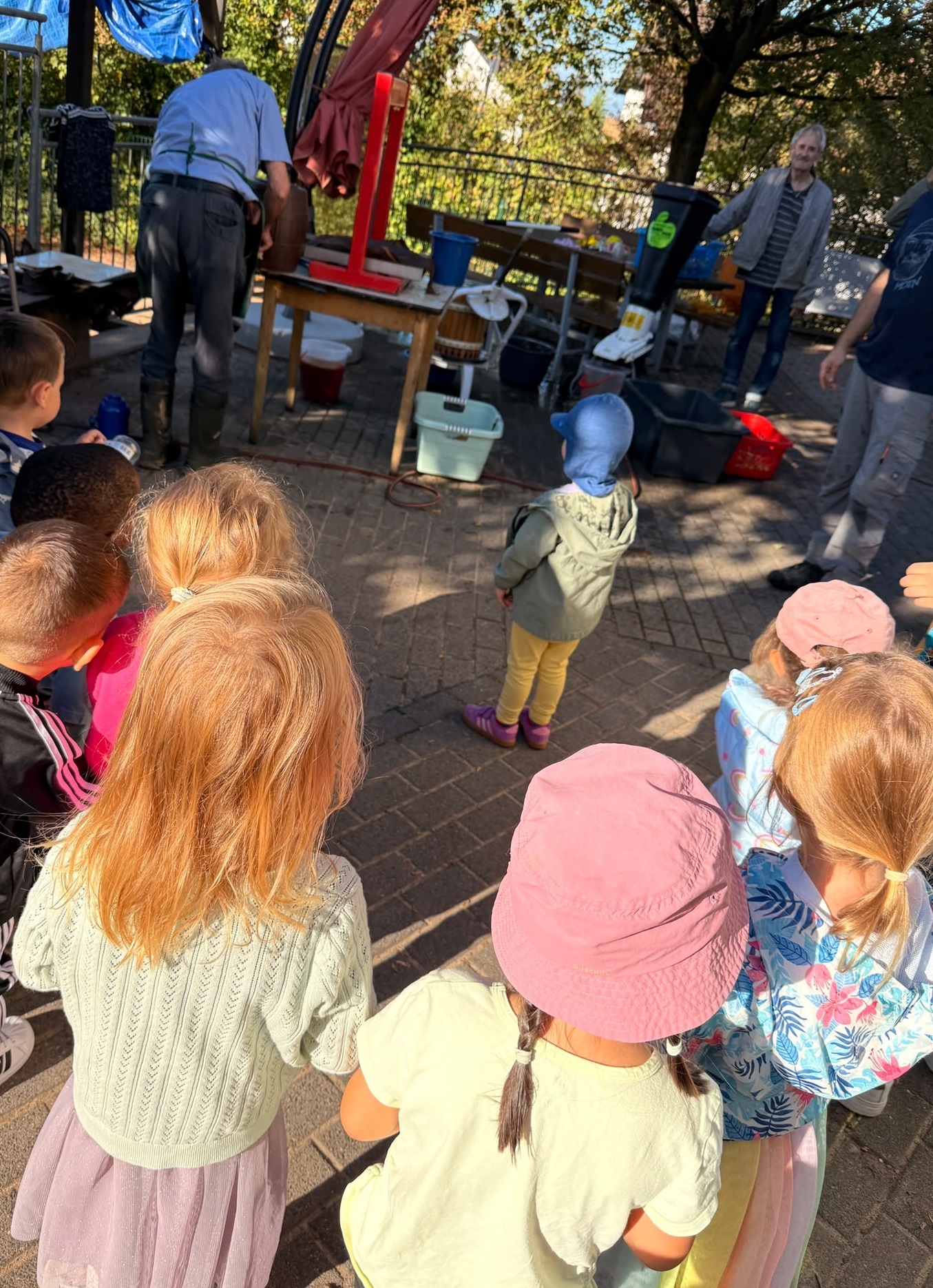 Kinder schauen einem Mann zu, wie er mit einer Apfelpresse Saft presst